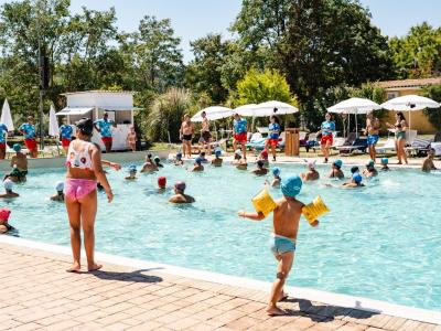 Bambini giocano felici in piscina sotto il sole estivo.