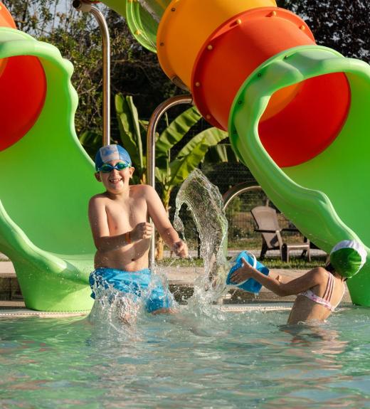 Bambini giocano in piscina con scivolo colorato.