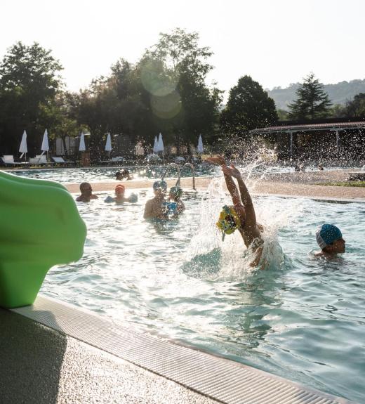 Bambini giocano in piscina sotto il sole estivo.