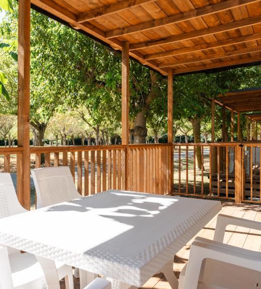 Terrazza in legno con tavolo bianco, immersa nel verde.