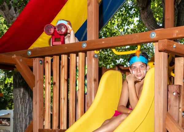 Bambini giocano su uno scivolo colorato in legno.