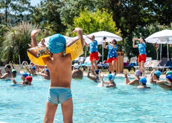 Bambino in piscina con braccioli, animatori sullo sfondo.