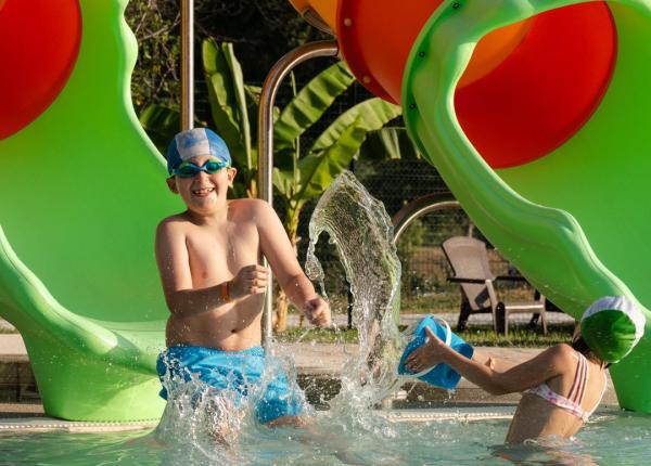 Bambini giocano in piscina con scivolo colorato.