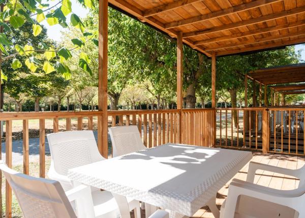 Terrazza in legno con tavolo bianco, immersa nel verde.