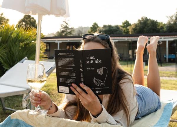 Donna legge un libro su una sdraio con un bicchiere di vino.