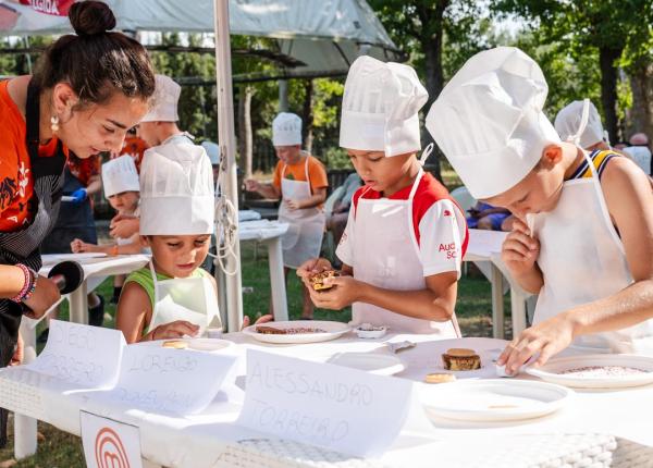 Bambini cucinano sotto un ombrellone durante un evento MasterChef Junior.