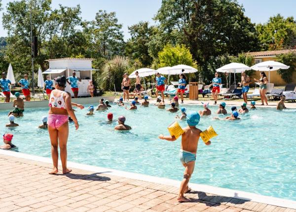 Bambini giocano felici in piscina sotto il sole estivo.