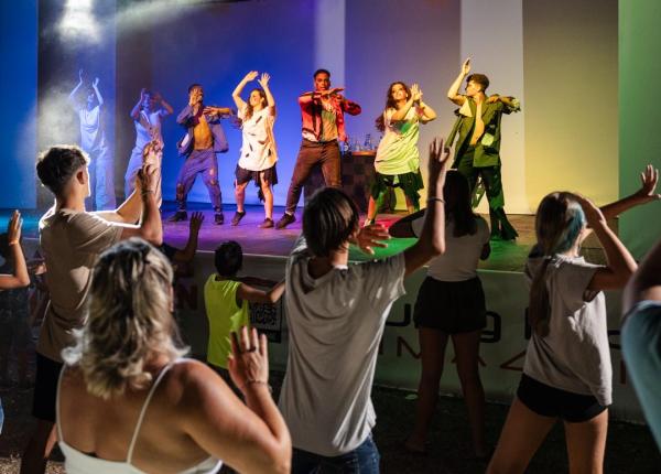 Spettacolo di danza energico, pubblico coinvolto e luci colorate sul palco.