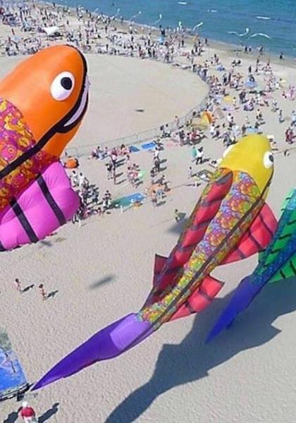 Festival di aquiloni a forma di pesce in una spiaggia affollata.