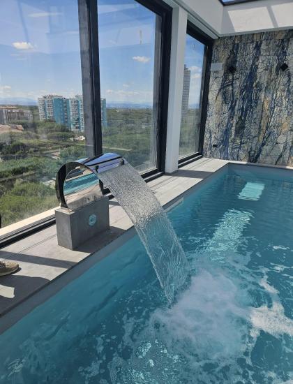 Piscina interna con cascata, vista mozzafiato sulla città e cielo azzurro.