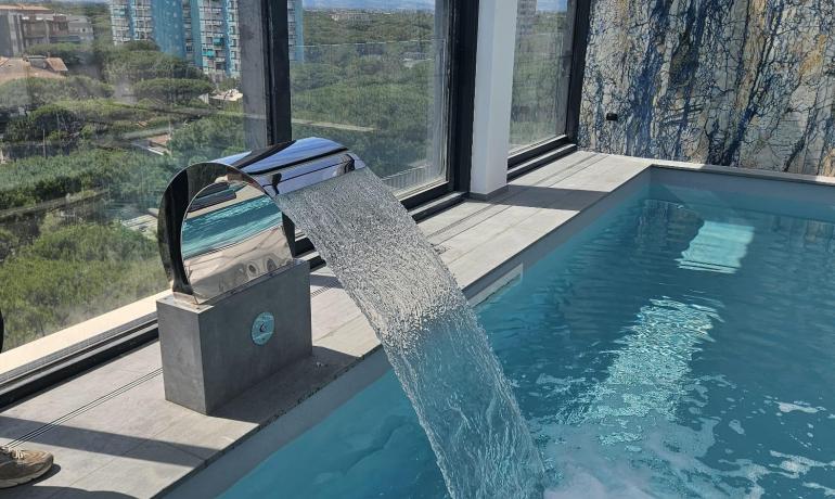 Piscina interna con cascata, vista mozzafiato sulla città e cielo azzurro.